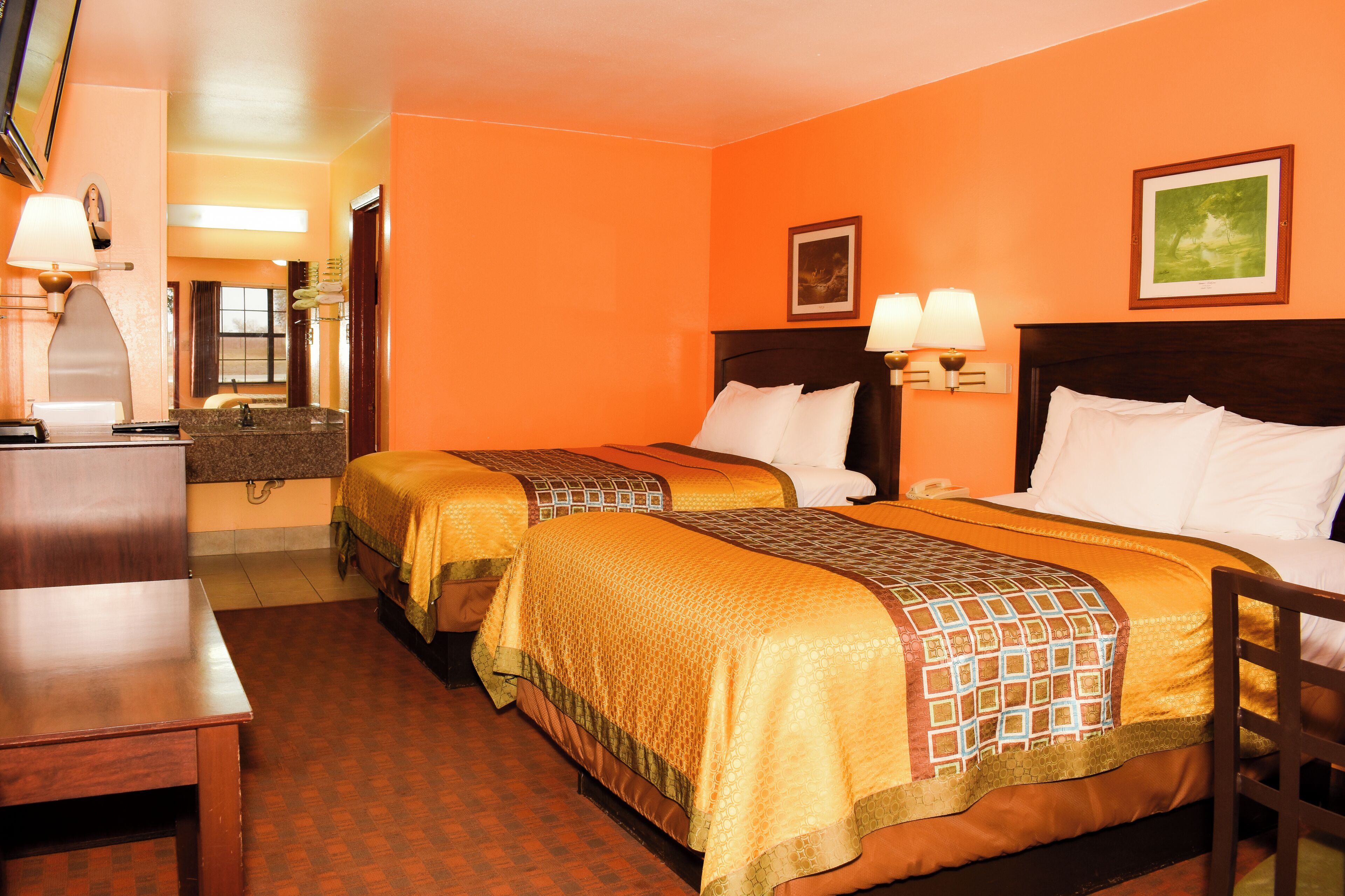 A hotel room with two beds, a desk, a chair, a mirror, and two wall-mounted lamps.