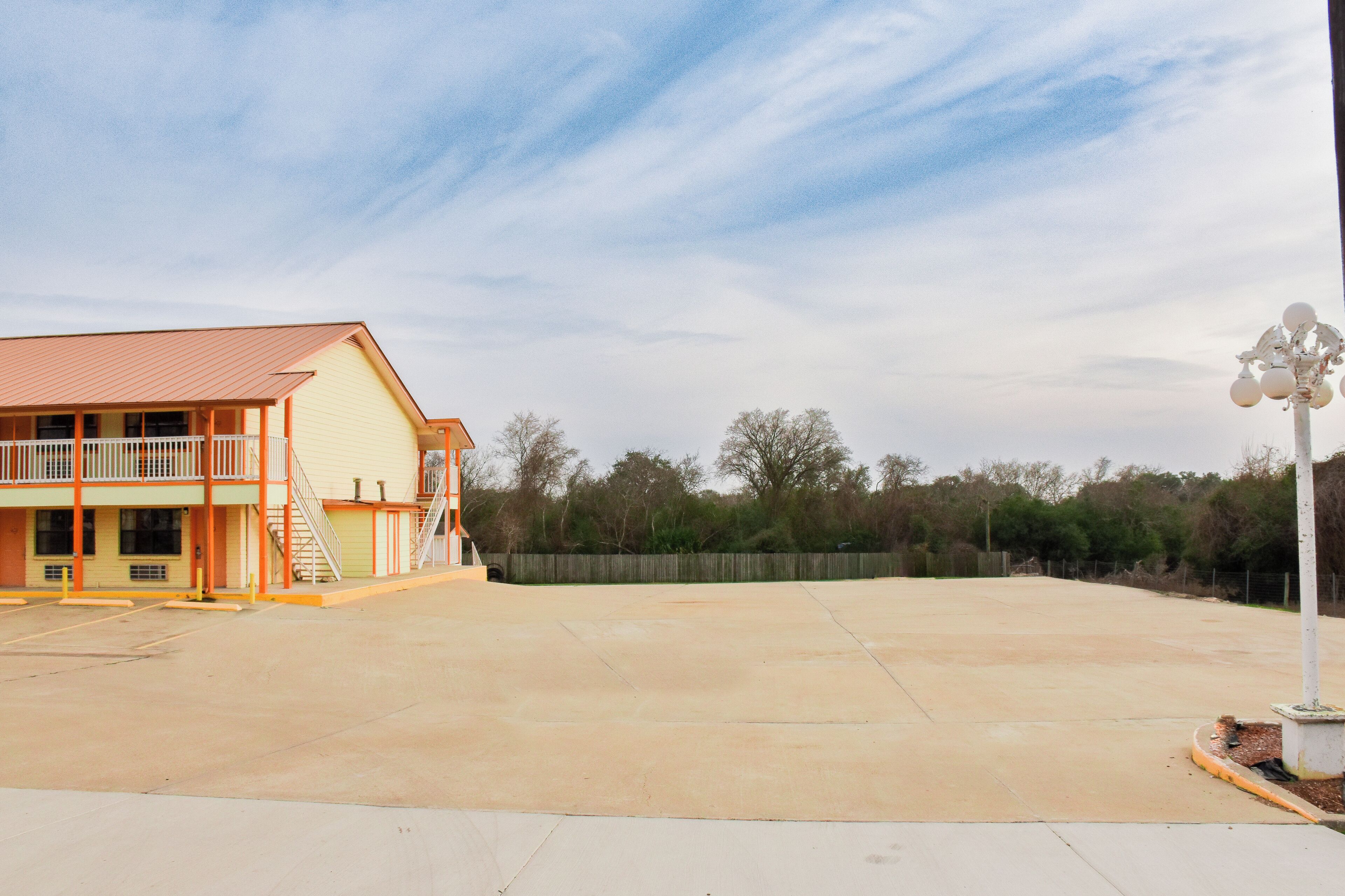 A building with a flat roof, a balcony, and a fenced parking area.