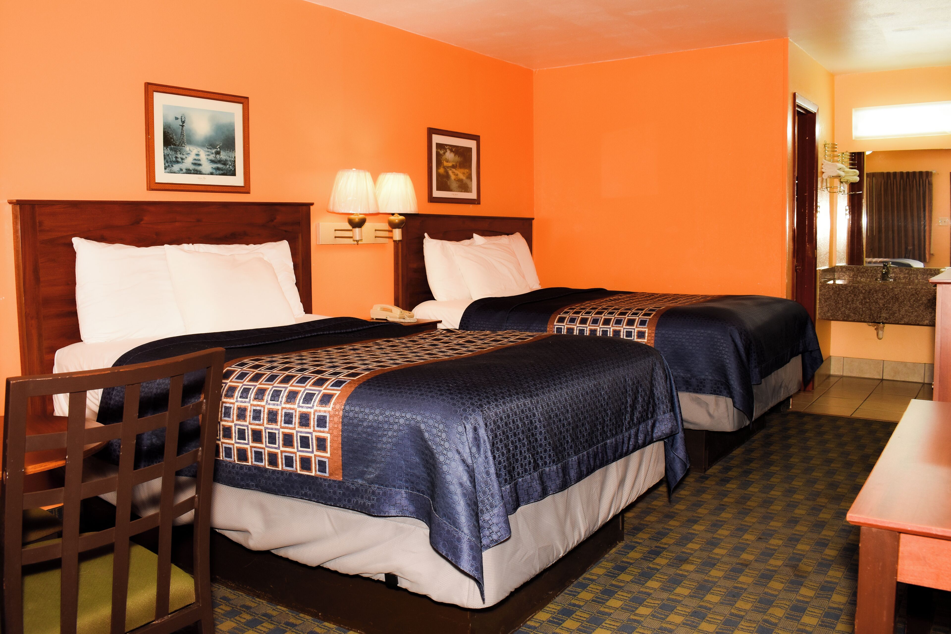 A hotel room with two beds, a wooden chair, a desk, and a bathroom visible through an open door.