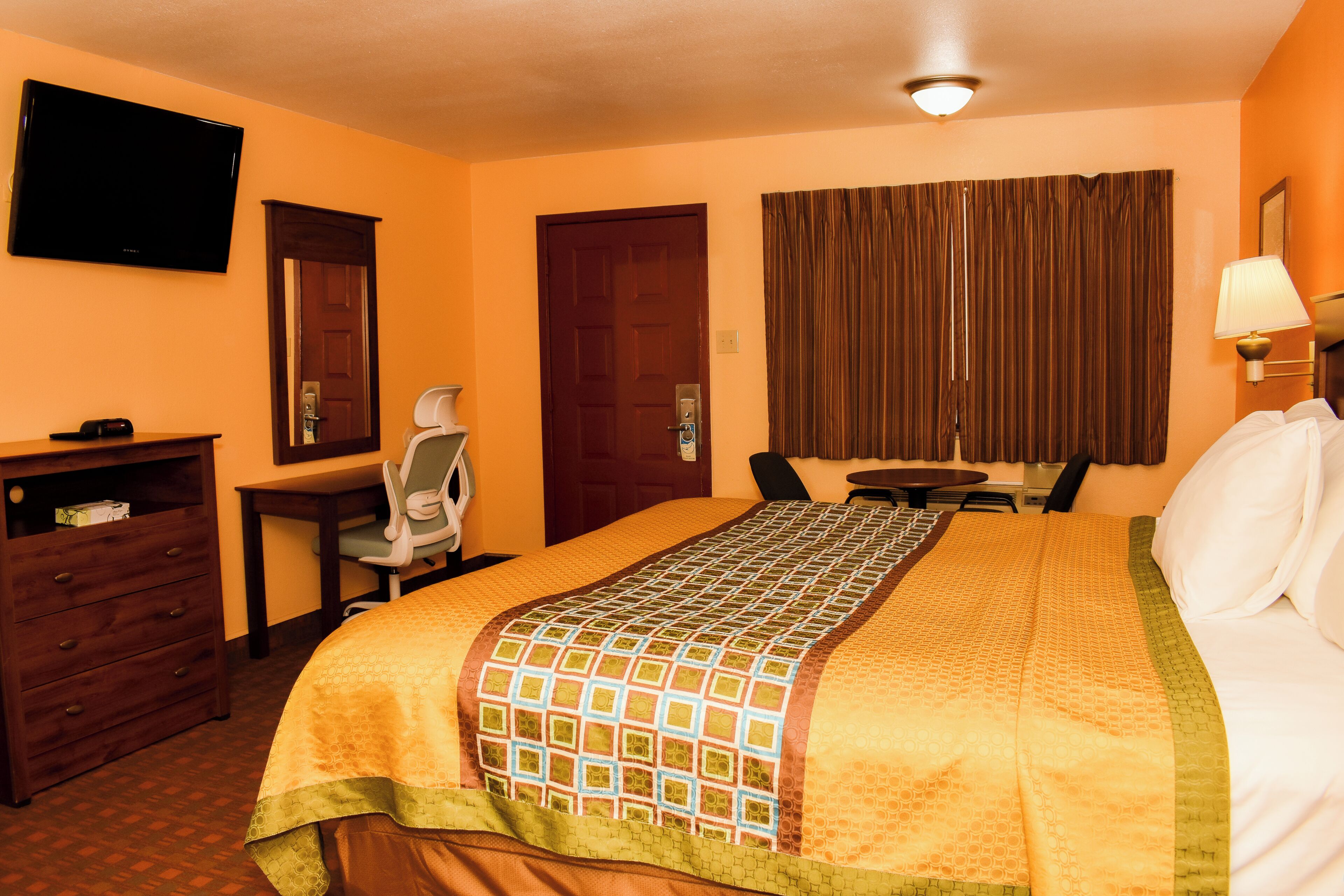 Una habitación de hotel con cama, escritorio, silla, televisión y puerta.