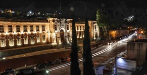 Un edificio histórico con arquitectura clásica, iluminado por farolas y luces provenientes de las ventanas.