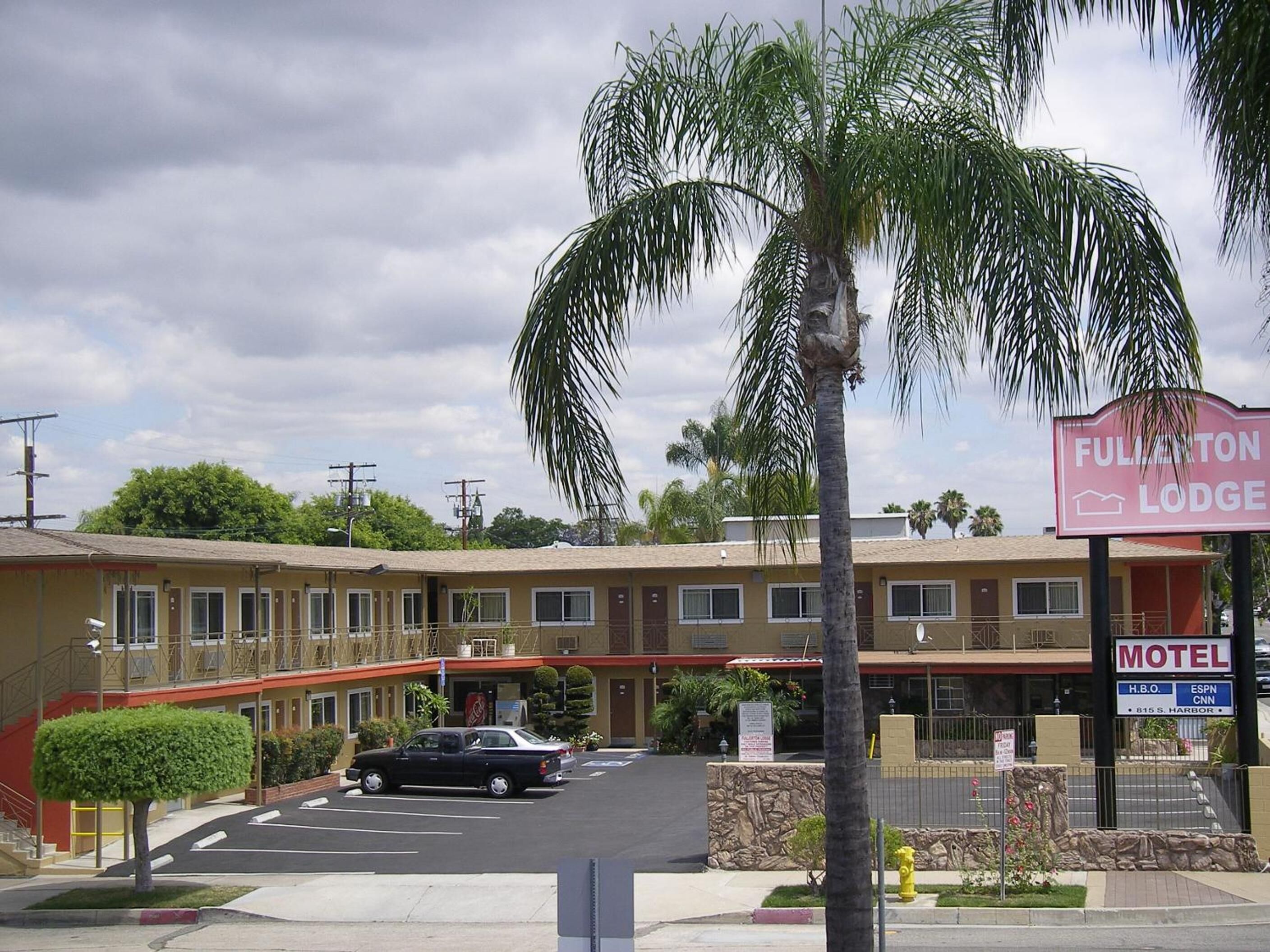 Un motel con un edificio a due piani, un parcheggio e una palma in primo piano.