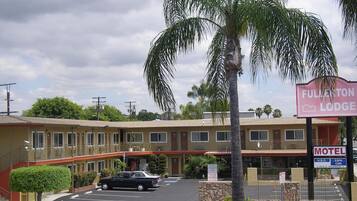 Un motel con un edificio a due piani, un parcheggio e una palma in primo piano.