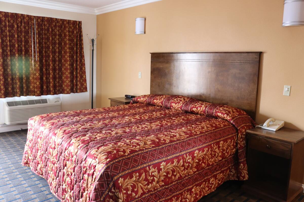 Une chambre d’hôtel avec un grand lit, une table de chevet avec un téléphone et une fenêtre avec des rideaux.