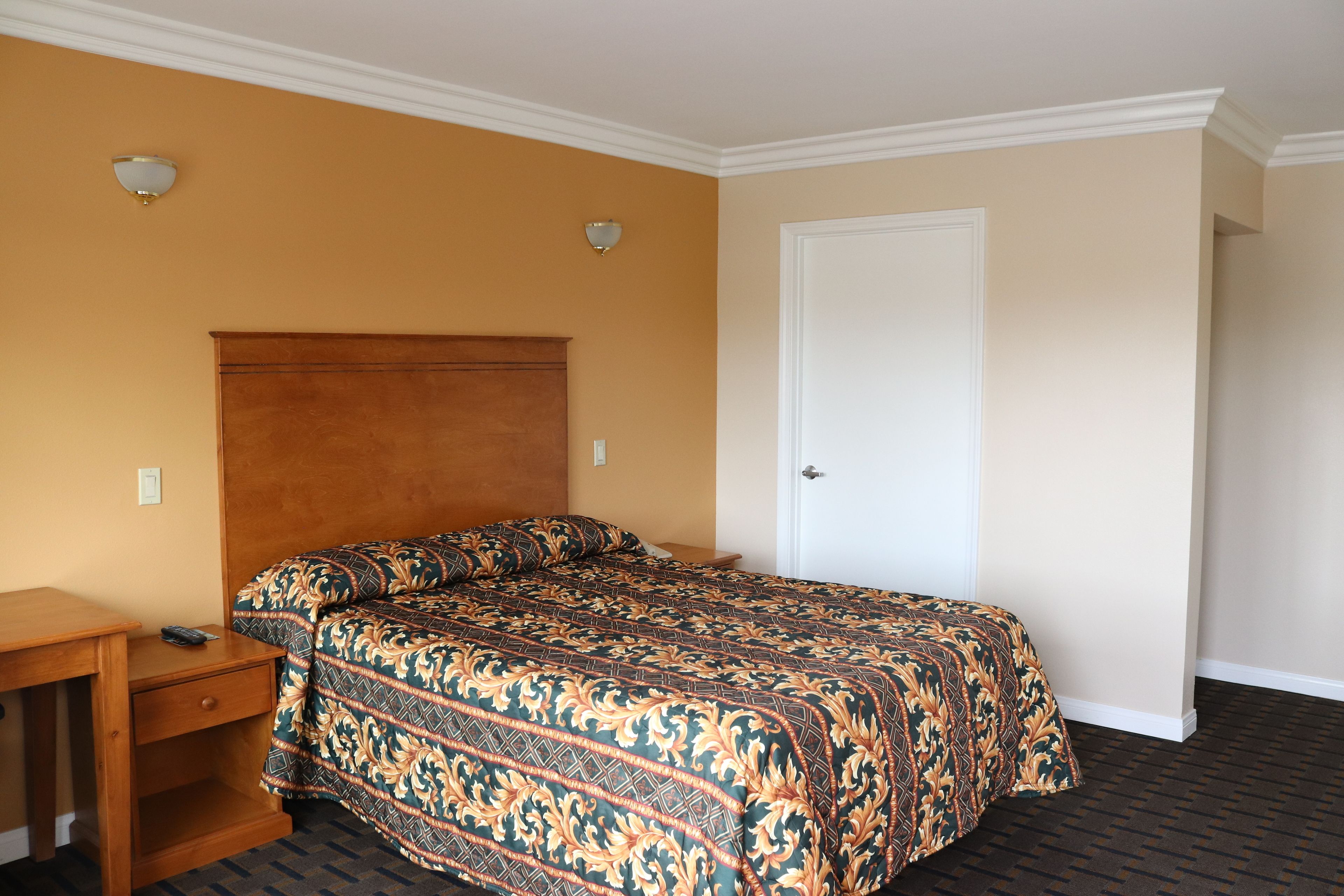 A hotel room with a large bed, a wooden nightstand, a desk, and a door.
