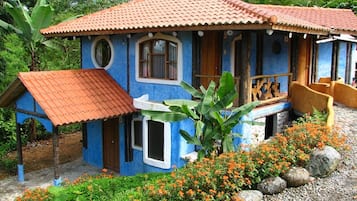 Ein Haus mit blauer Fassade und rotem Ziegeldach, umgeben von einem Garten mit orangefarbenen Blumen und Steinen.