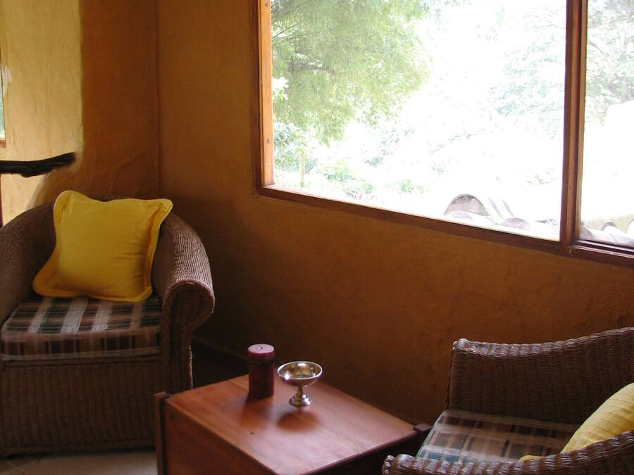 A cozy room with wicker furniture, a wooden coffee table, and a large window offering a view of greenery outside.