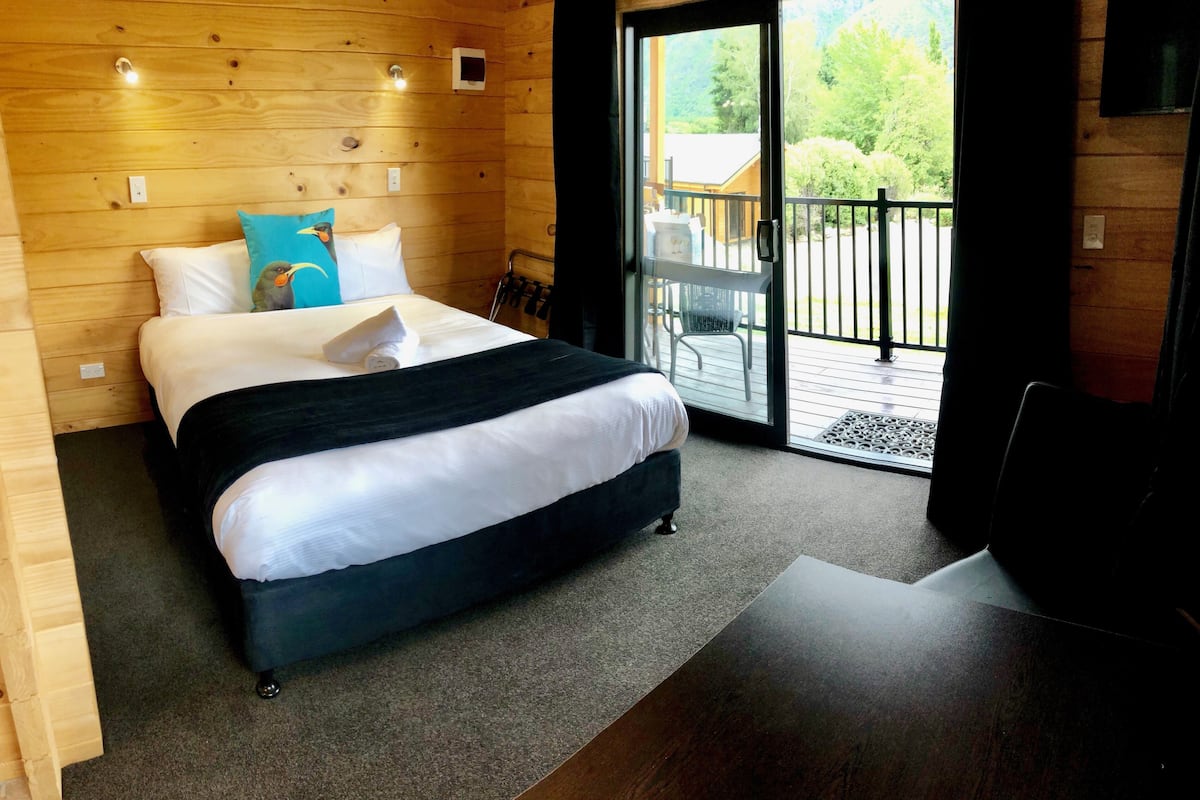 A wooden-paneled bedroom with a bed, a view of the outdoors, and a balcony.