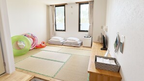 Quarto com tatames, futon, uma pequena mesa com chaleira, televisão e janela com cortinas.