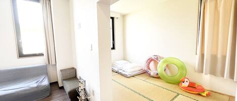 Una habitación con una cama tipo futón, un sofá futón, una mesita y un sillón futón. Se ven dos camas tipo futón.