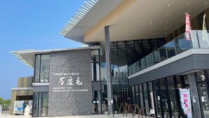 Um edifício moderno com fachada de vidro ampla, uma placa vertical de destaque com texto e céu claro.