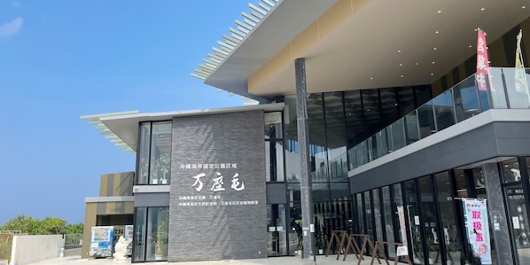A modern building with a large glass facade, a prominent vertical sign with text, and a clear sky. - LOW COST RESORT MANZA BEACH (Onna)