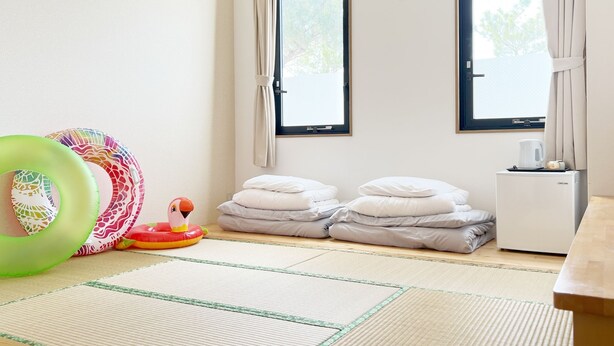 Quarto com tatames, um frigorífico pequeno e uma mesa de madeira com chaleira e chávenas.