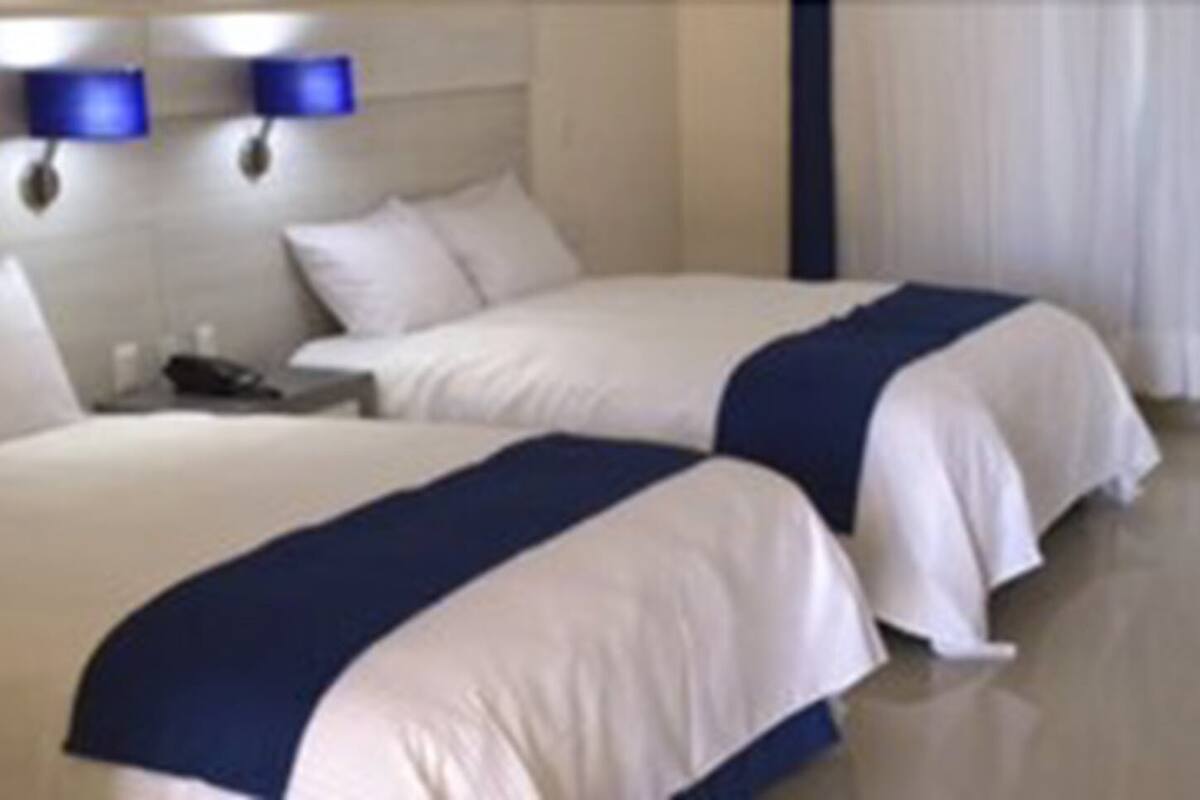 Habitación de hotel con dos camas, una mesita de noche y una ventana con cortinas.