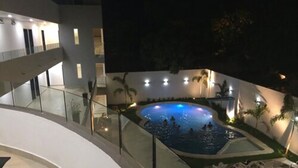 A nighttime view of a hotel with a swimming pool, glass railings, and outdoor seating. - MH Grand Hotel (Ometepec)