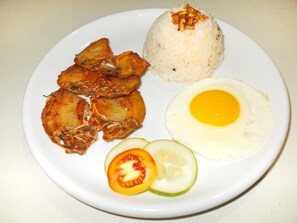 A plate with fried fish, rice, a fried egg, and sliced vegetables.
