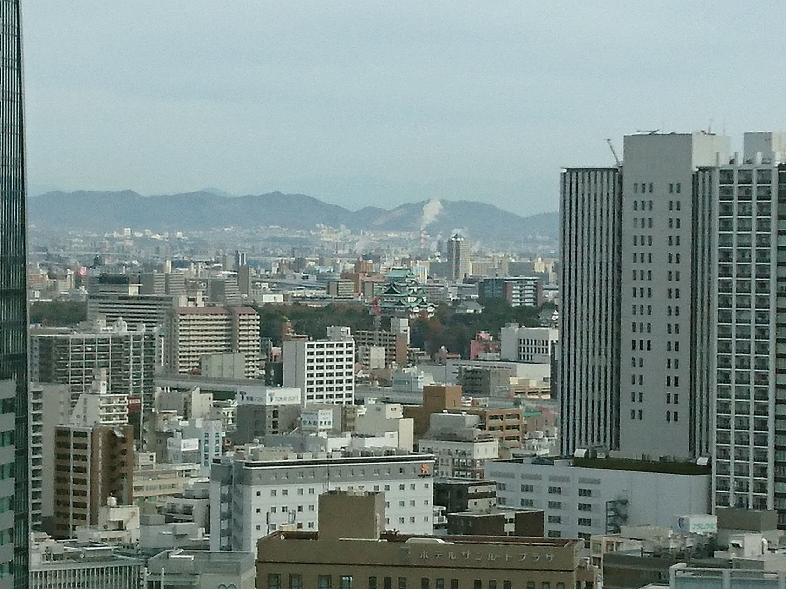 Paisagem urbana com diversos edifícios, incluindo um arranha-céu branco imponente e um edifício tradicional com telhado verde.