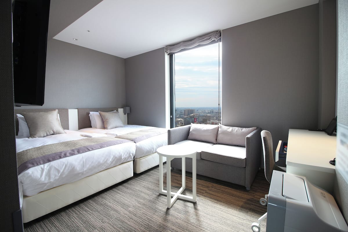 A modern hotel room with two beds, a sofa, a small table, and a desk with a computer.