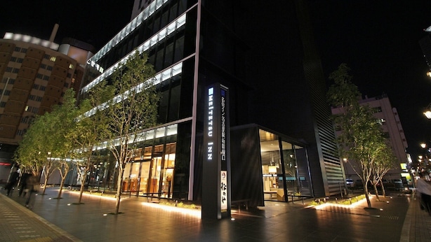 Un hotel moderno con facciata in vetro, area salotto esterna e ingresso ben illuminato.