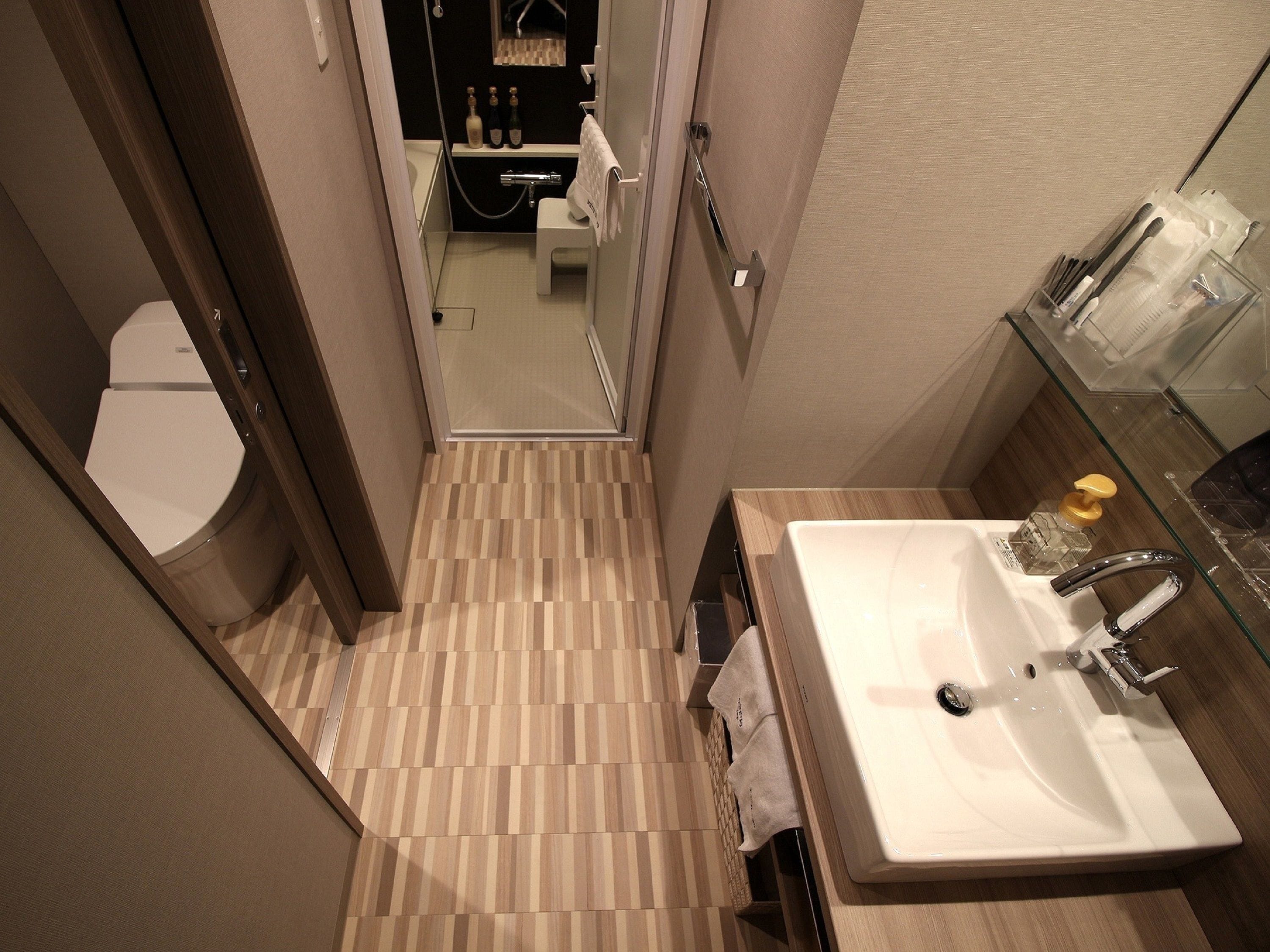 A modern bathroom with a wooden floor, a white sink, and a glass shower enclosure.