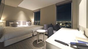 Una camera d'albergo con due letti, un tavolino e vista sulla città illuminata di notte.