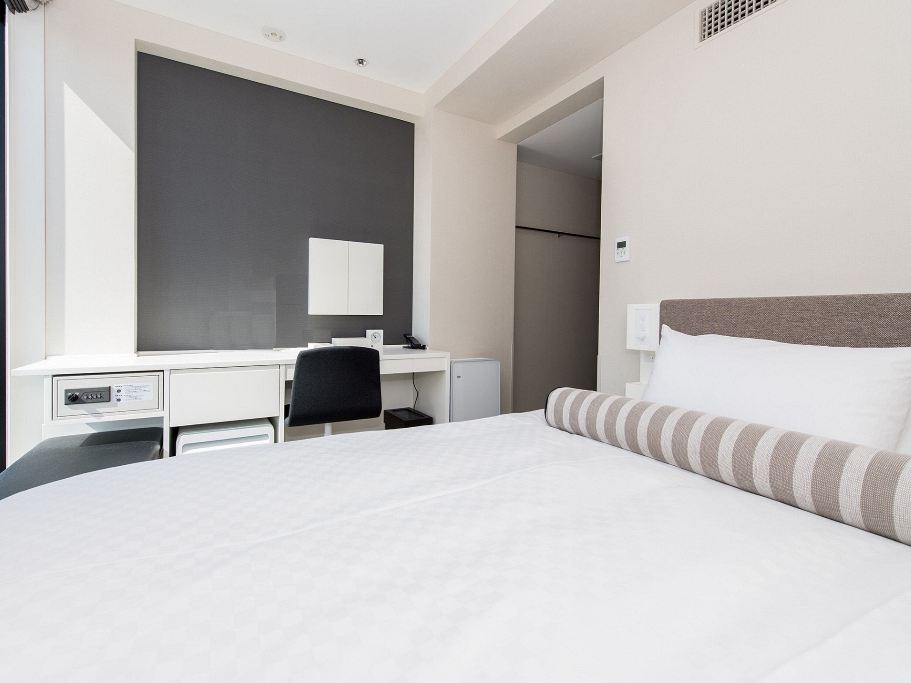 A hotel room with a bed, a desk, a chair, a mirror, and a wardrobe.