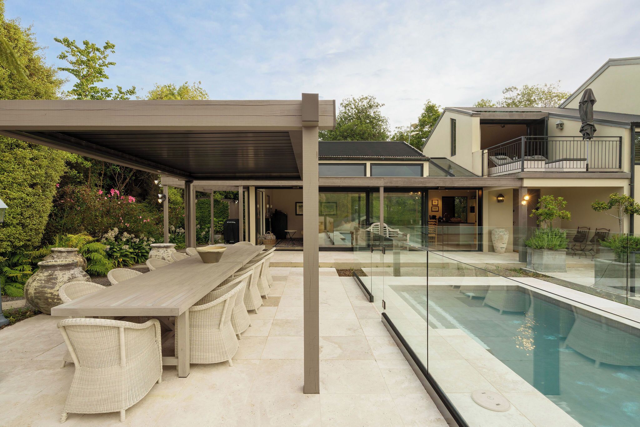 Een modern huis met een overdekte patio, een zwembad en een eethoek met rieten meubilair.