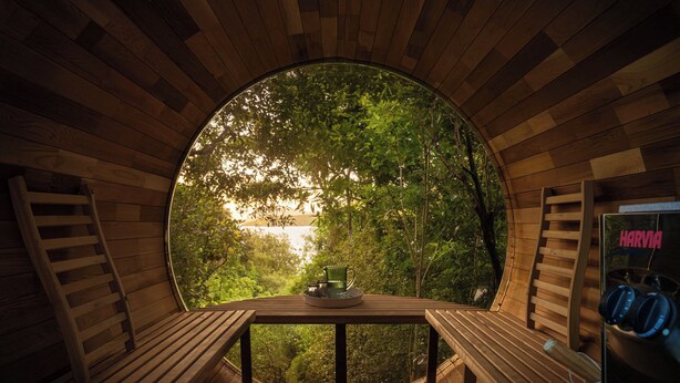 A circular wooden room with a table and benches, a ladder, and a view of a forest. - The Point Villas (Taupo)