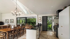 A modern kitchen with a central island, dining area with wooden chairs, and a view through the glass door. - The Point Villas (Taupo)