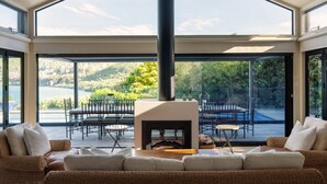 A spacious living room with a fireplace, large windows, and a view of a lake and hills. - The Point Villas (Taupo)