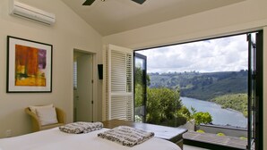 A bedroom with a large bed, a window with blinds, a view of a river, and a framed picture on the wall. - The Point Villas (Taupo)