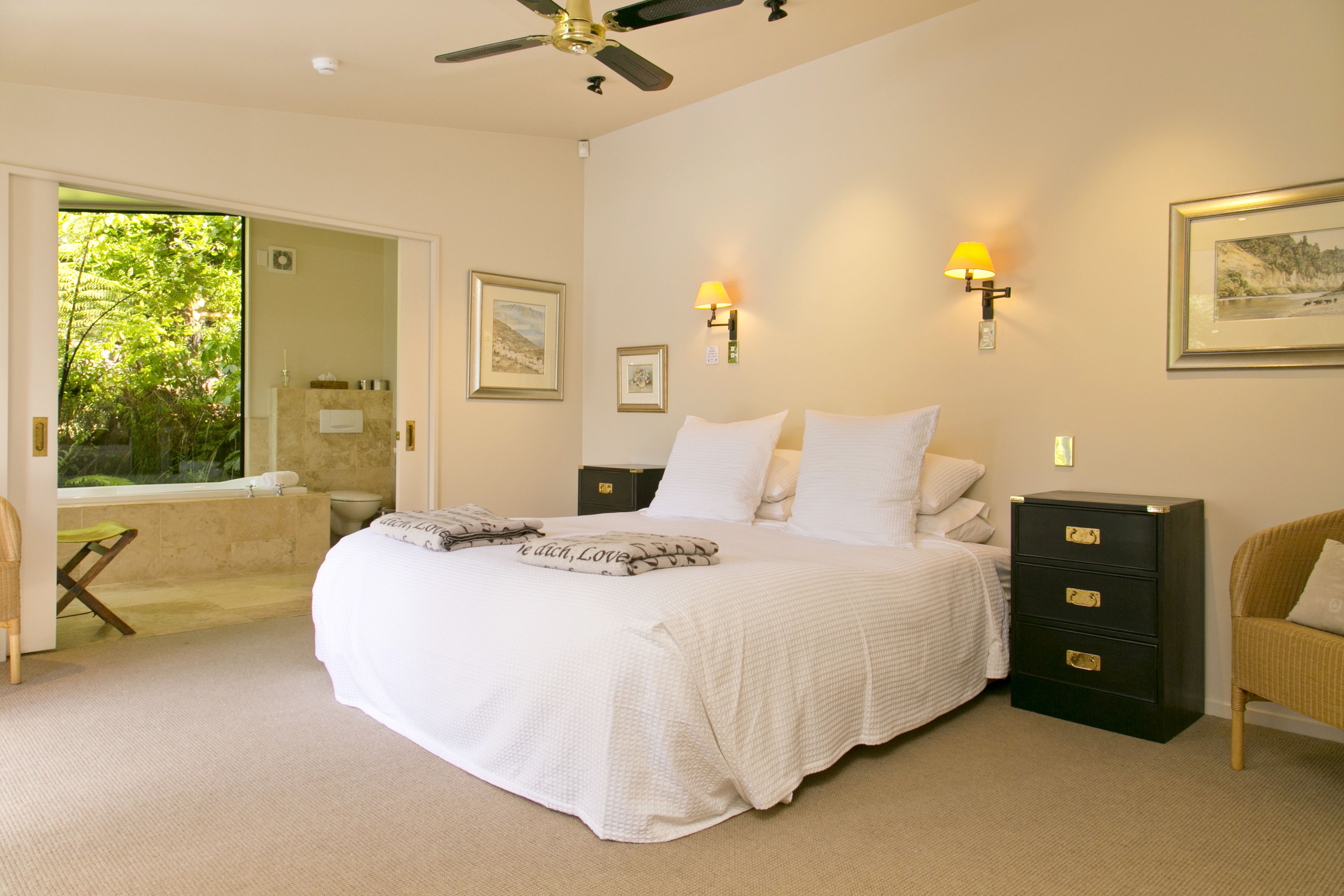 Une chambre spacieuse avec un grand lit, une table de chevet, une commode et une chaise. Une fenêtre offre une vue sur la verdure environnante.