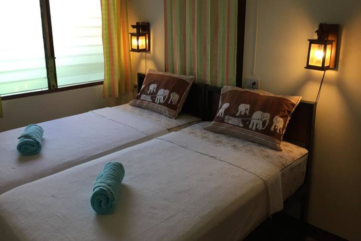 A hotel room with two beds, each with a pillow featuring elephant designs, and two wall-mounted lamps.
