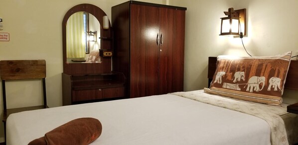 A hotel room with a bed, a wooden wardrobe, a mirror, a wall-mounted lamp, and a decorative pillow. - Siriwan Guesthouse (Chiang Mai)