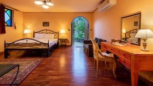 A hotel room with a bed, desk, chair, and a view through an archway to an outdoor area. - Davinci Di Khao Yai (Pak Chong)