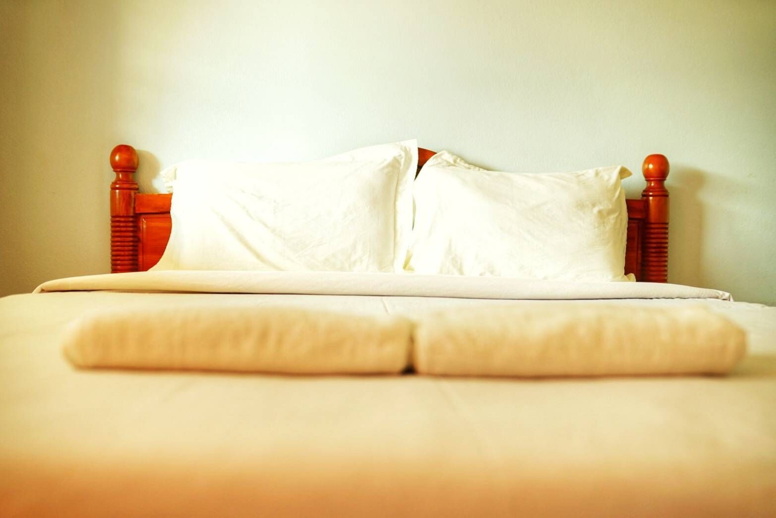 Una cama bien hecha con sábanas blancas y patas de cabecera de madera.