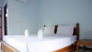 A neatly made bed with white linens and two towels, a wooden headboard, and a small wooden nightstand. - Tararin (Chiang Saen)