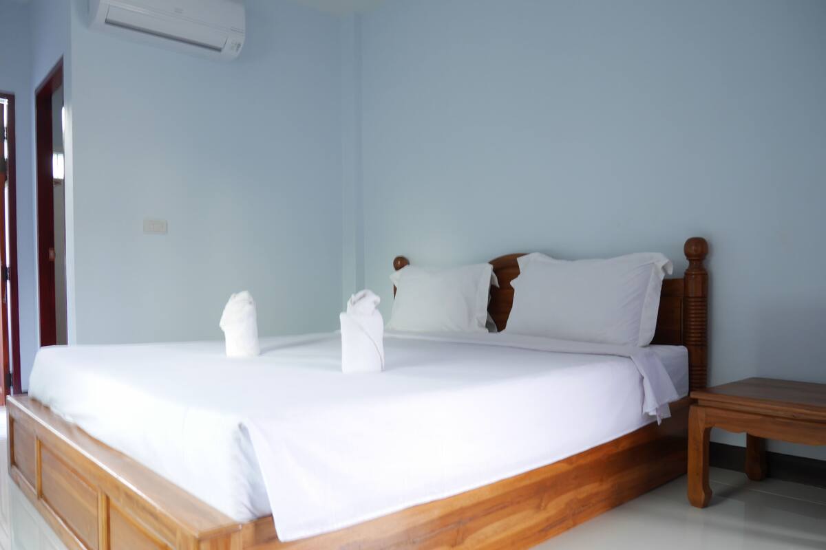 A neatly made bed with white linens and two towels, a wooden headboard, and a small wooden nightstand.