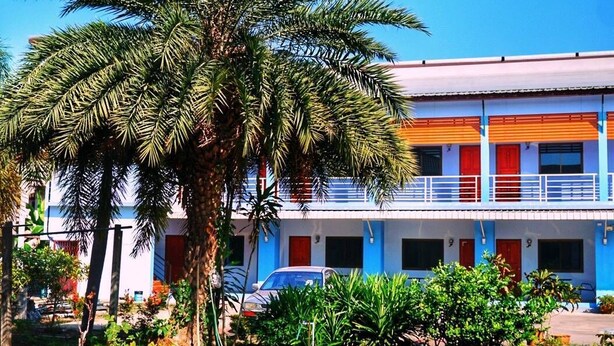 A building with a blue and white facade, a palm tree in front, and a parking area. - Tararin (Chiang Saen)