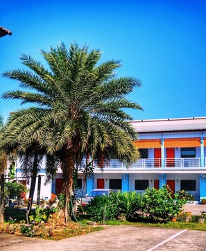 A building with a blue and white facade, a palm tree in front, and a parking area. - Tararin (Chiang Saen)