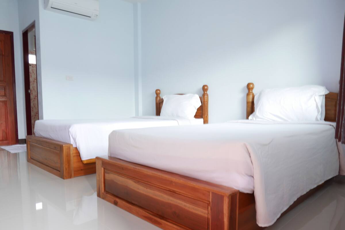 A double bed with wooden headboards, a small wooden bench, and a white wall with an air conditioning unit.