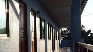 A covered corridor with a tiled floor and wooden doors, leading to an open area with a view of trees. - Tararin (Chiang Saen)