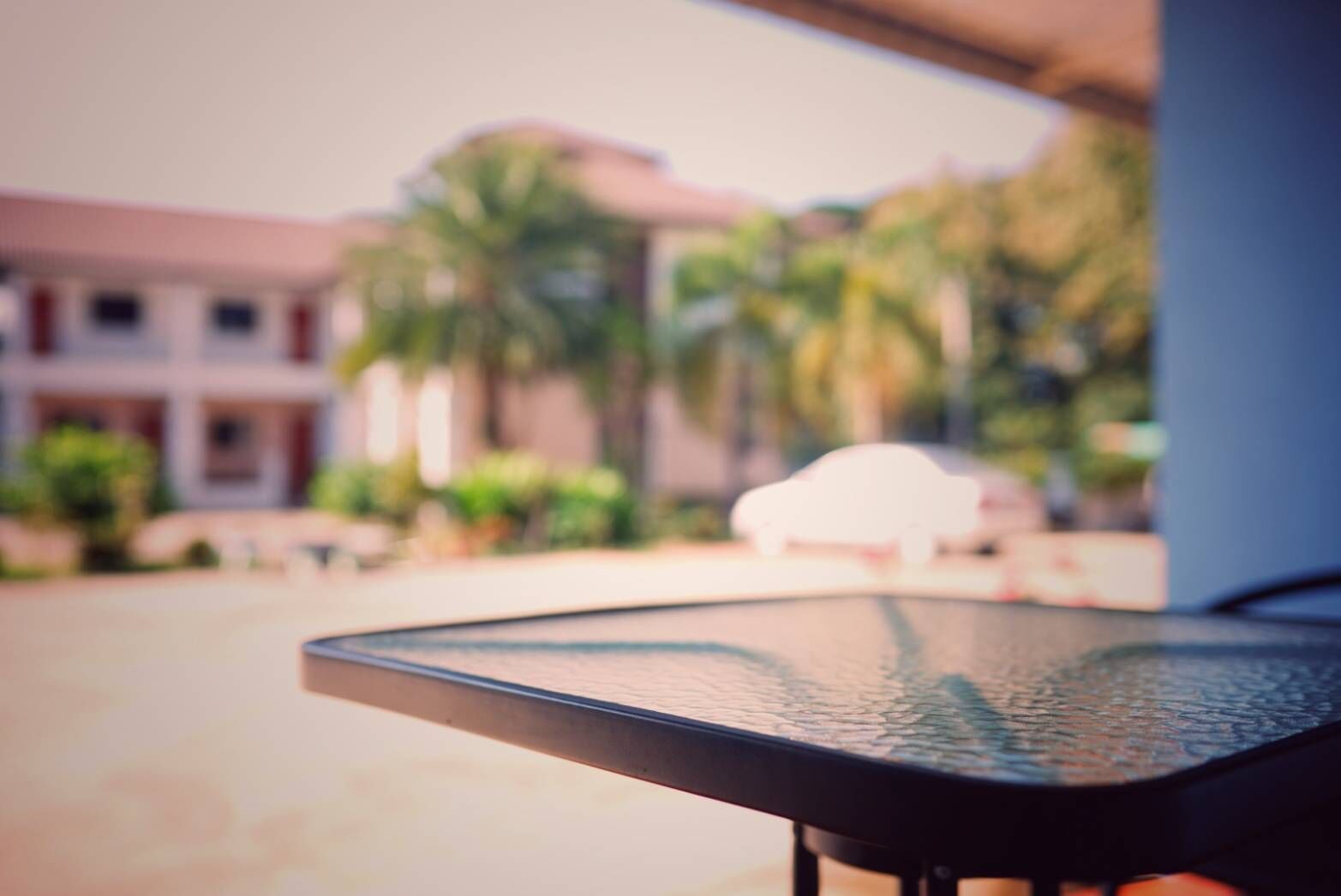 A blurred view of a building with a balcony, palm trees, and a white chair.
