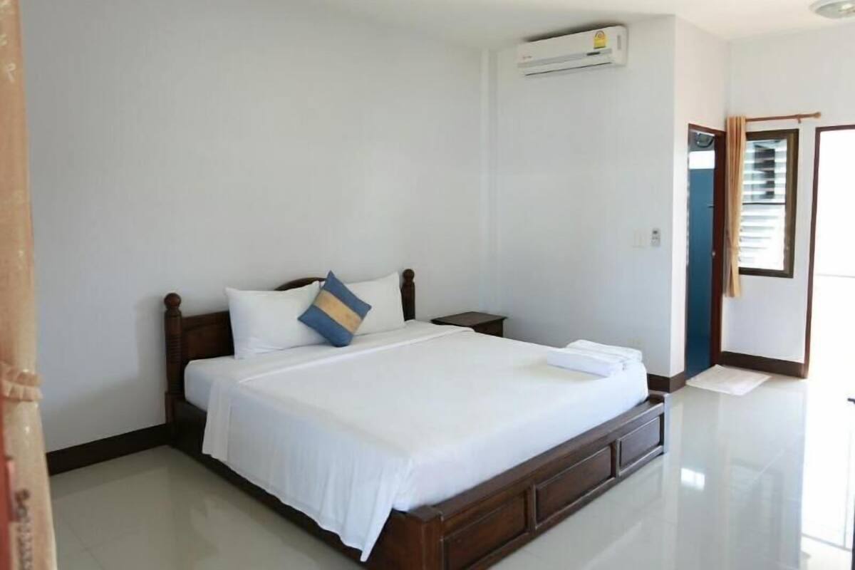 A bedroom with a bed, a nightstand, an air conditioning unit, and a door with a curtain.