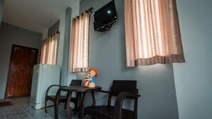 A dining area with a table and chairs, a television mounted on the wall, and a refrigerator in the background.