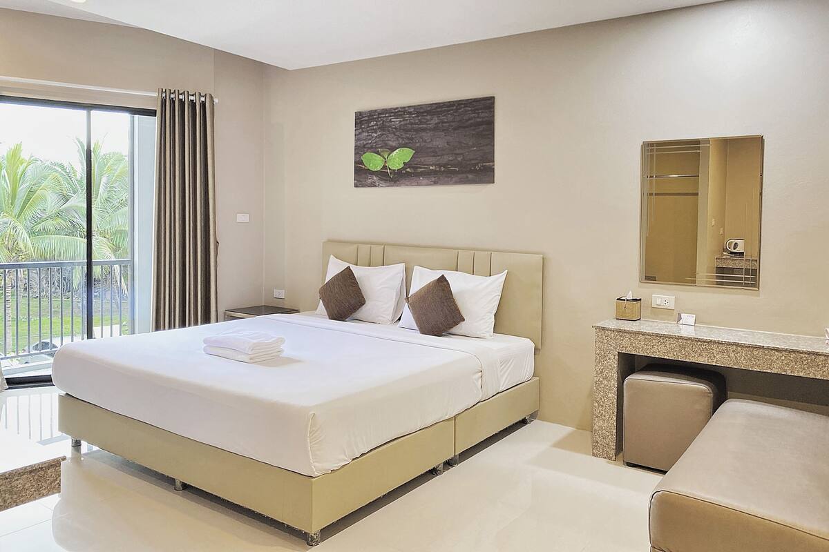 A hotel room with a large bed, a bathroom with a mirror, and a view of palm trees through the window.