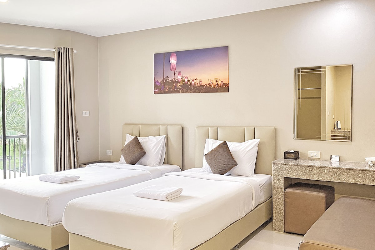 A hotel room with two beds, a small desk, a mirror, and a window with curtains.