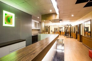 Ett modernt receptionsområde med en receptionsdisk i trä, en grön, upplyst skylt och träningsutrustning i bakgrunden.