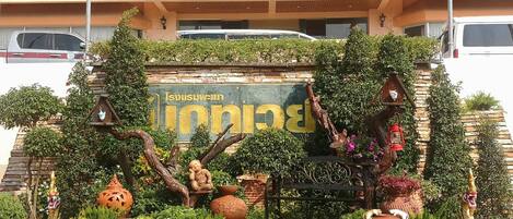 Un jardín con un letrero que dice "Baan Nakhon Si Thammarat", rodeado de plantas y elementos decorativos.