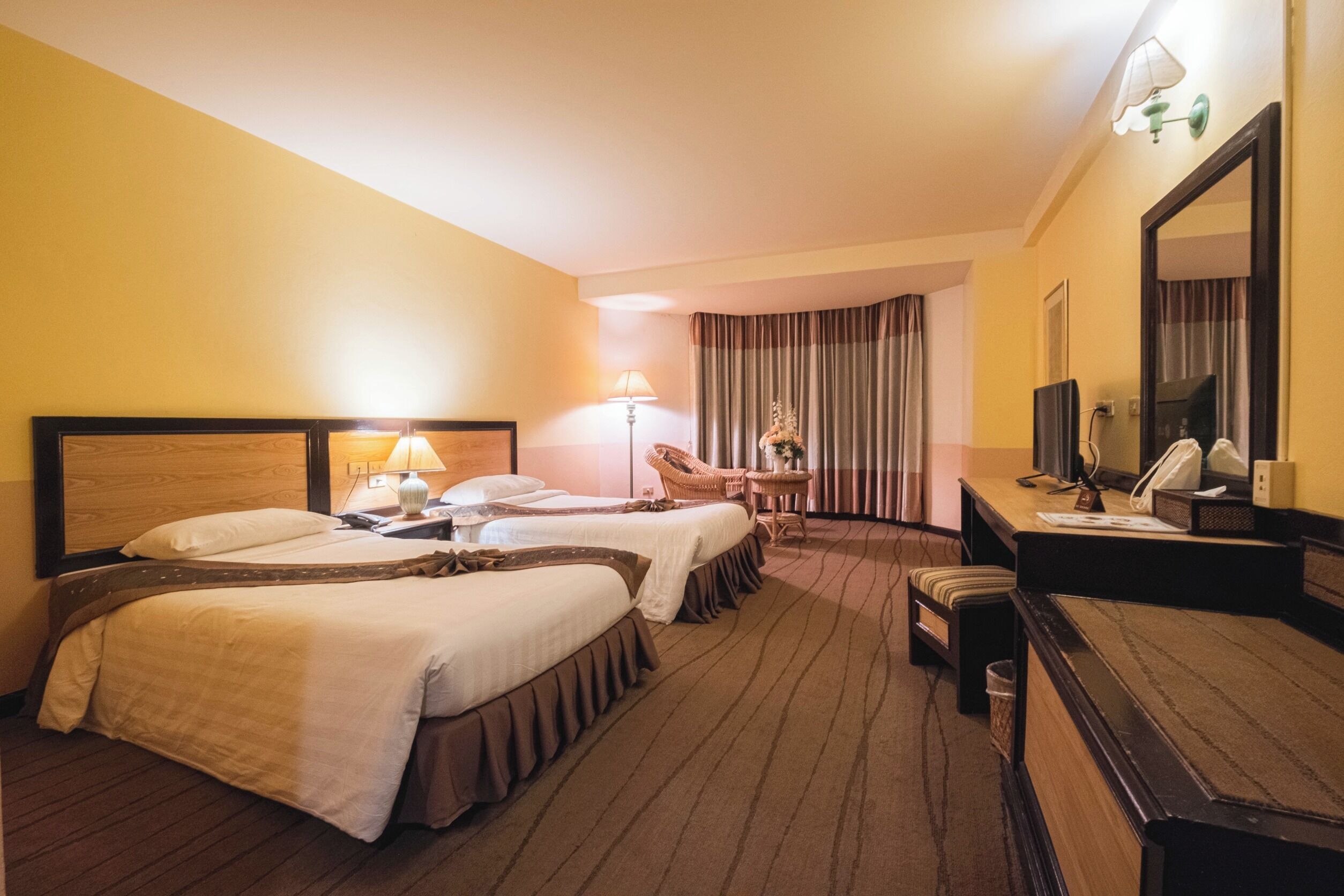 Quarto de hotel com duas camas, uma escrivaninha com cadeira, televisão e espelho.